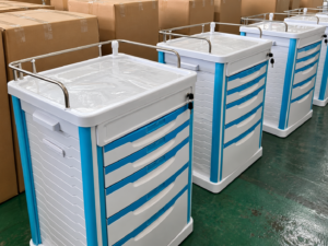 Blue and white medical carts beside cardboard cartons for crash cart shipping